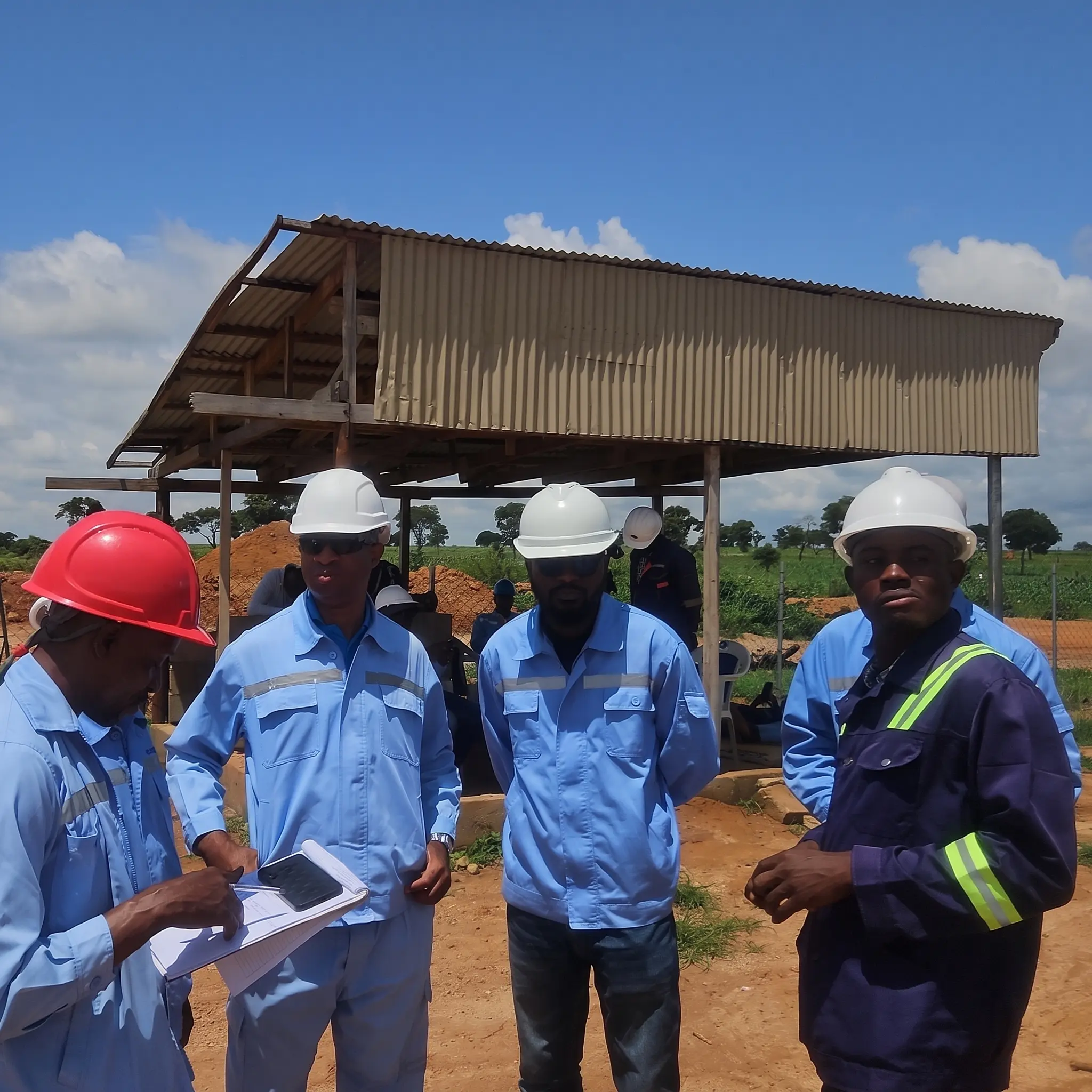 Field personnel in hard hats and reflective workwear reviewing documents together at a construction site.