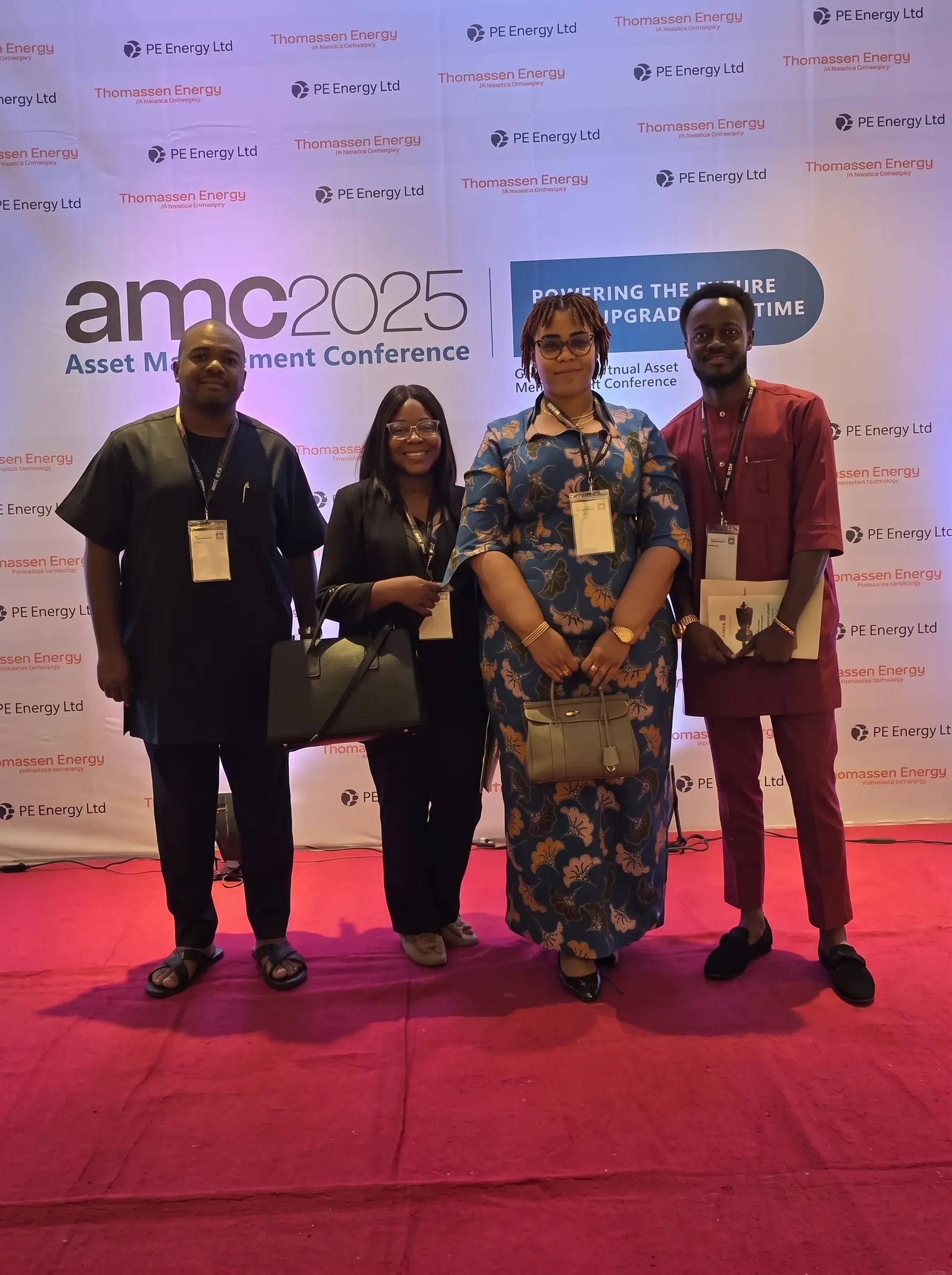 Four attendees at the 2025 Asset Management Conference, standing in front of the event backdrop.